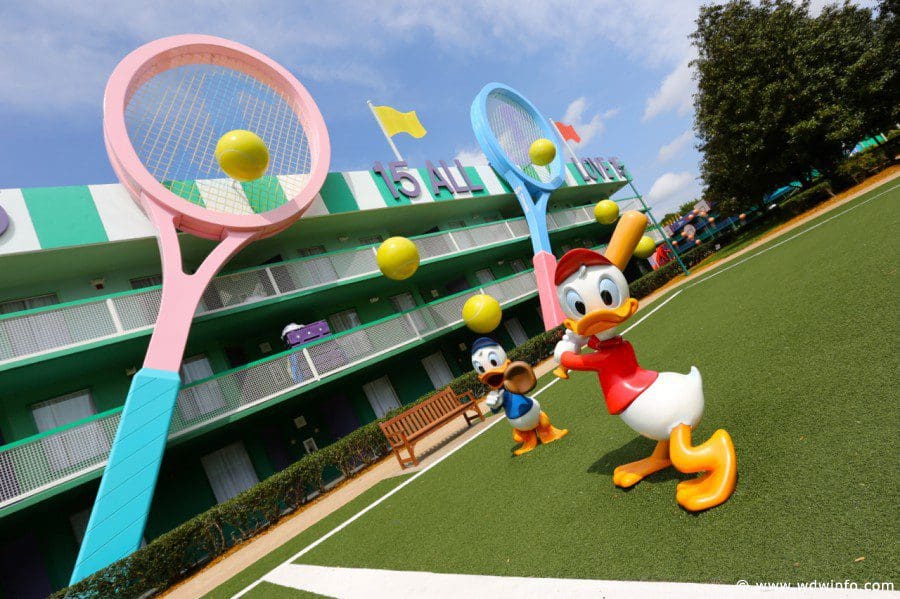 A statue of Donald Duck plays tennis near a hotel building at Disney’s All-Star Sports Resort, with the appearance of a tennis court.