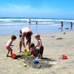 A dad and three kids plan in the sand on a beach near San Diego.