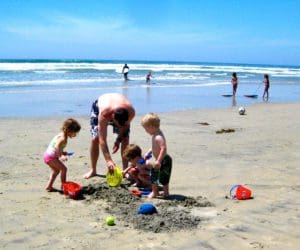 A dad and three kids plan in the sand on a beach near San Diego.