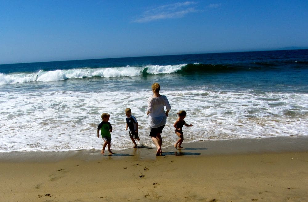 A mom and her three kids run along the beach and waves in San Diego.
