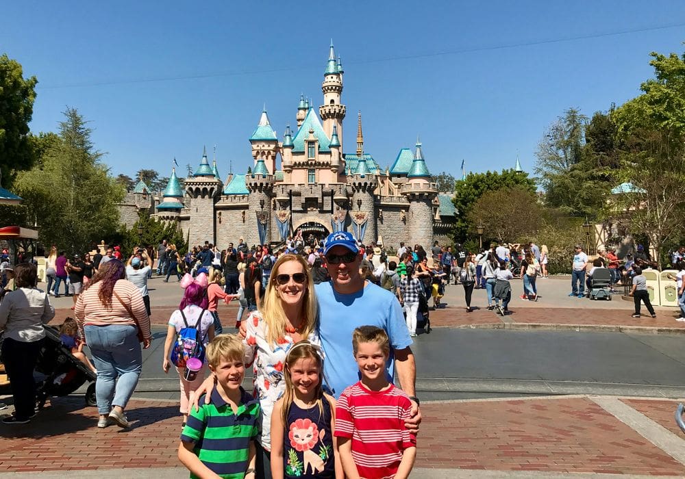 Two parents and their three kids stand together with the Disneyland castle behind them.