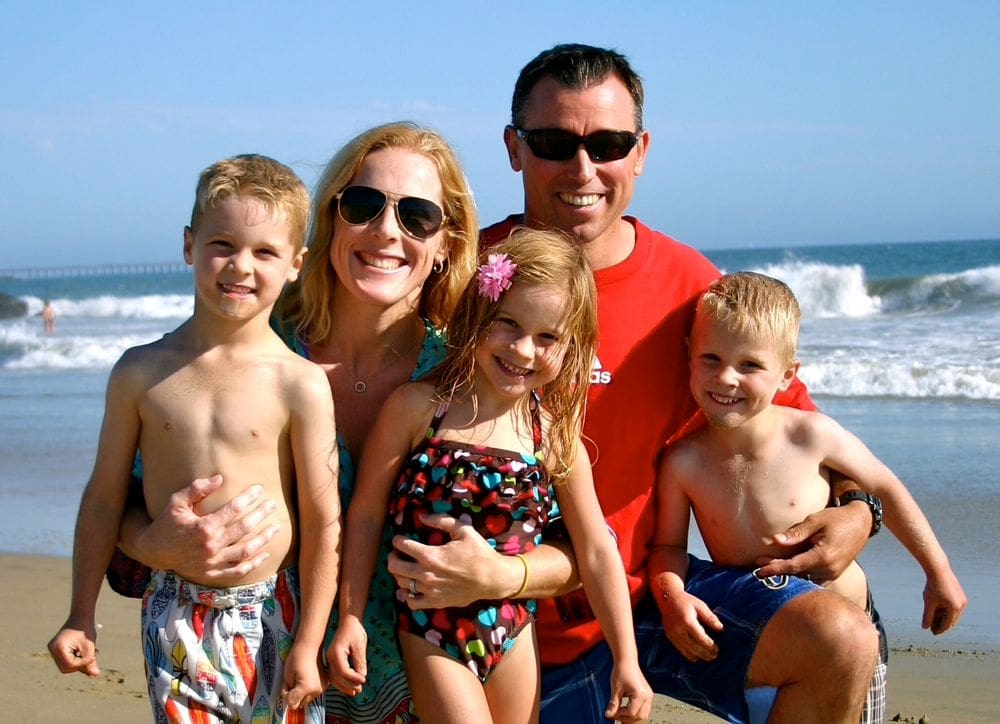 A family of five smiles together while enjoying a beach day.