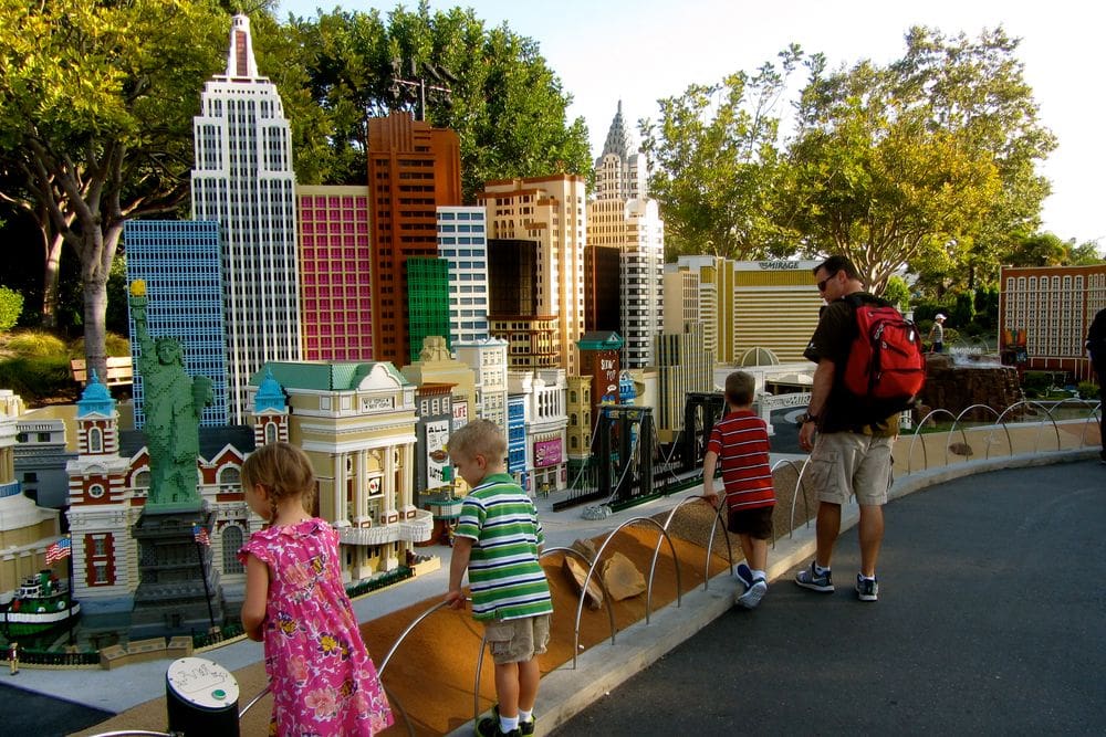 A dad and his three kids enjoy a lego display of NYC while exploring Legoland in San Diego, one of the best US cities for a Memorial Day Weekend with kids.