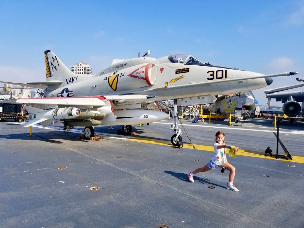 A young girl strikes a pose with a Navy plane behind her at USS Midway.