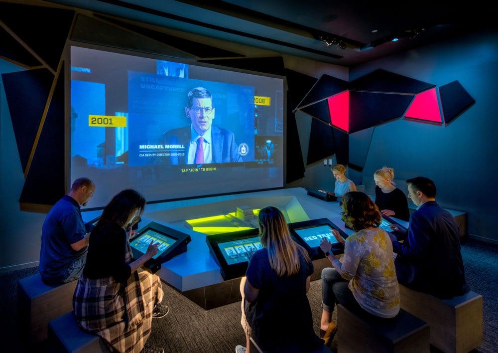 A number of people sit at an interactive exhibit at the International Spy Museum, one of the best DC museums for kids.