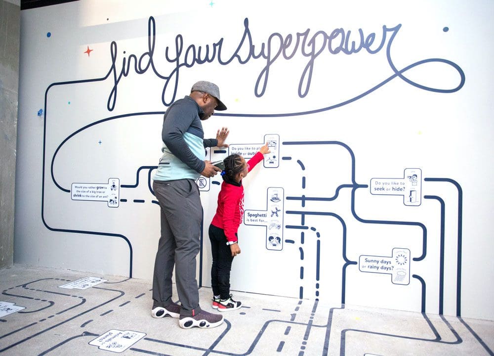 An African American man and his daughter interact with a hands-on exhibit about super powers at the National Children’s Museum, one of the best DC museums for kids.