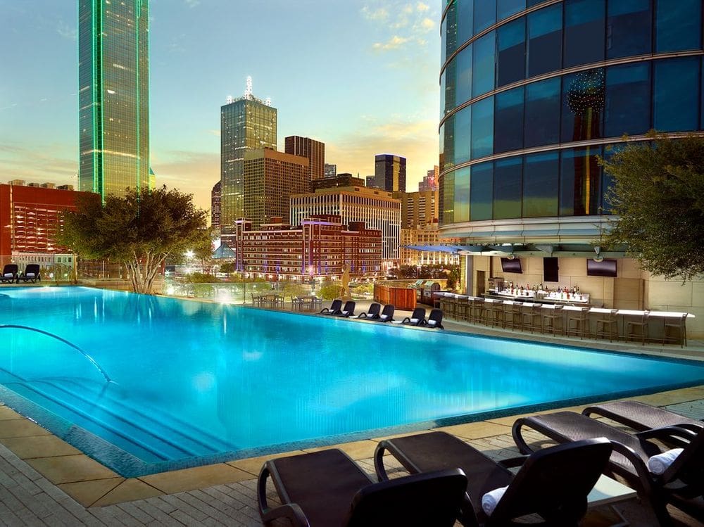 The outdoor pool at the Omni Dallas Hotel at night, featuring a skyline view and poolside bar.
