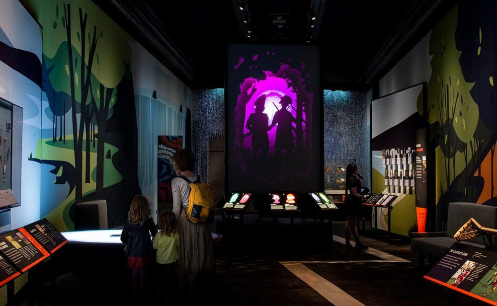 A mom and her two young children look at an exhibit in a darkened room at the Smithsonian National Museum of the American Indian, one of the best DC museums for kids.