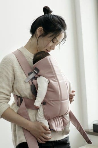 An Asian woman holds her infant in a BABYBJÖRN Baby Carrier Mini on her front.