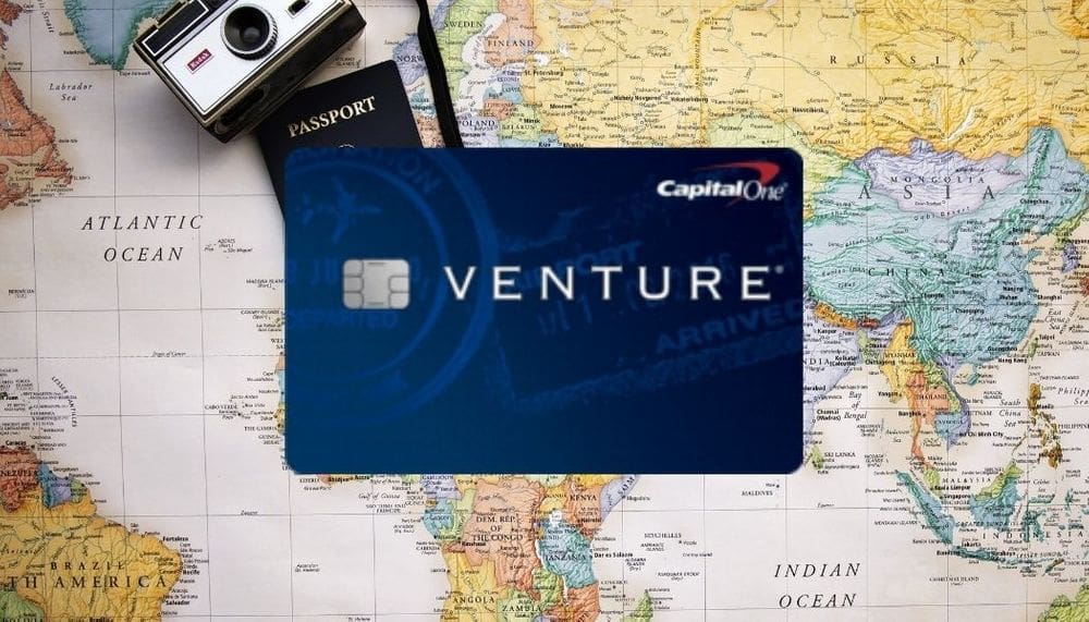 A close up of a CapitalOne Venture Rewards credit card, nestled on a background of a map, featuring a camera and passport.