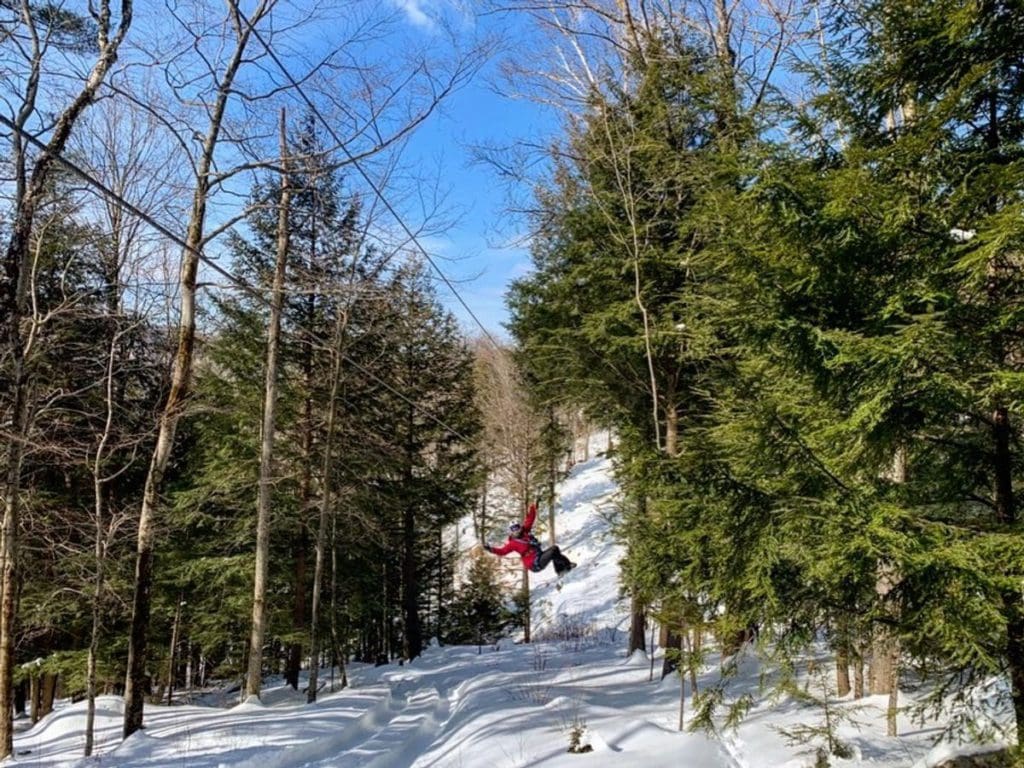 A person in a red coat soars down a zipline above the snow with Alpine Adventures.