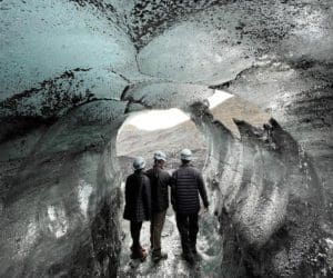 A family of three explore a cave while on a tour in Iceland.