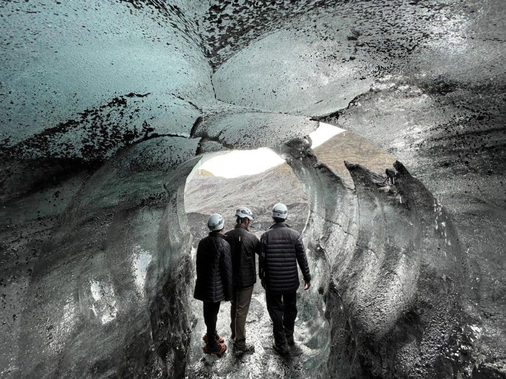 Three people explore the entrance to a cave in Iceland.