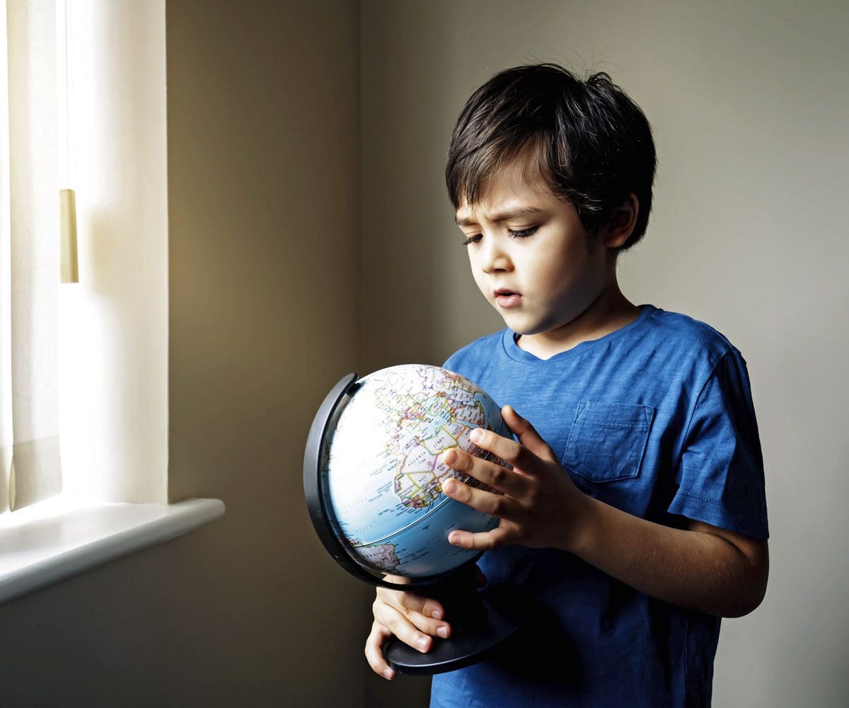 A young boy holds a globe near a window.