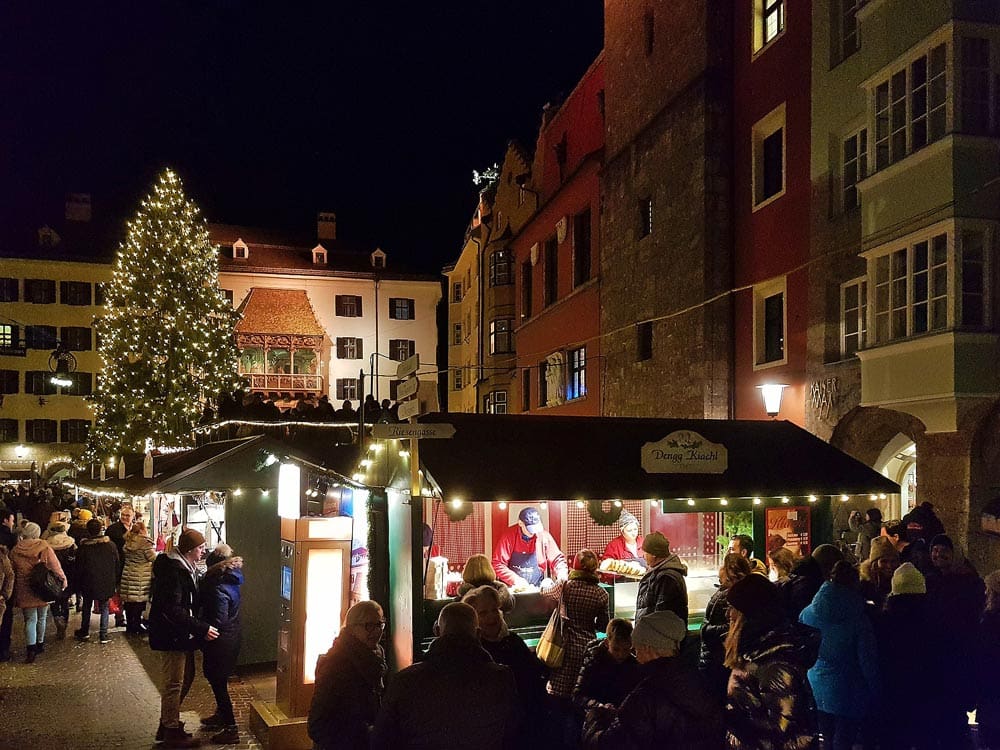 People wander about the Innsbruck Christmas Market, featuring several stalls and large Christmas tree.