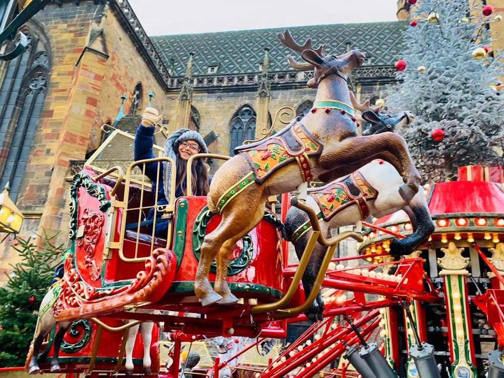 A young girl waves from a reindeer and slide ride at the Colmar Christmas Market.