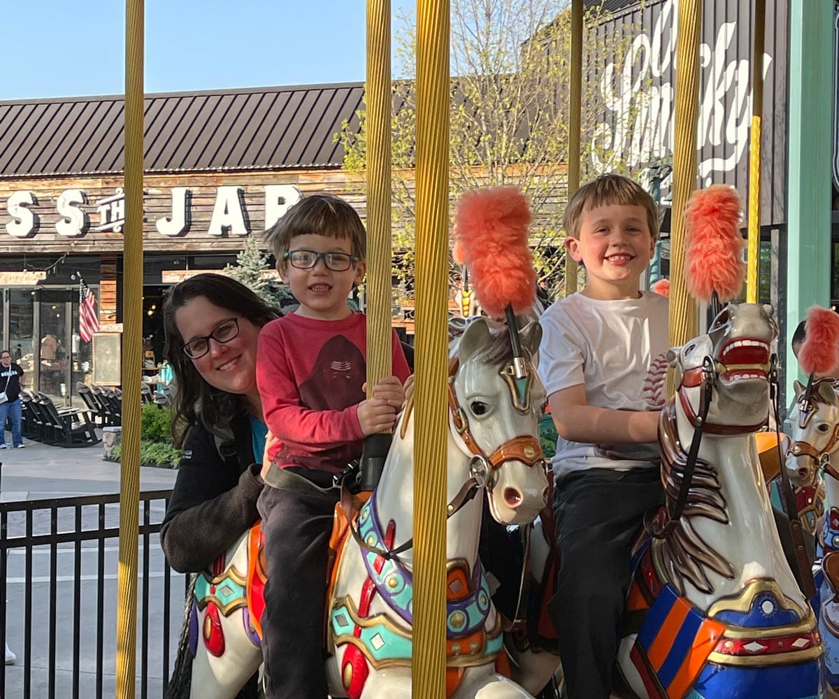A mom and her two sons enjoy a carousel near Gatlinburg, one of the best affordable summer vacations in the United States with kids.
