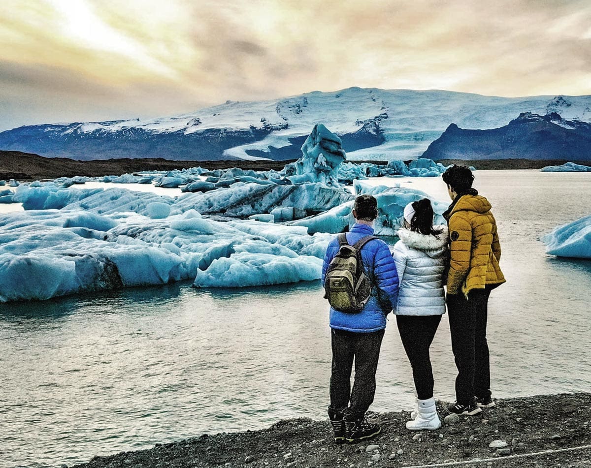Three teens stand together looking at the Jökulsárlón Glacier Lagoon in Iceland, one of the top places in travel in 2023 with kids.