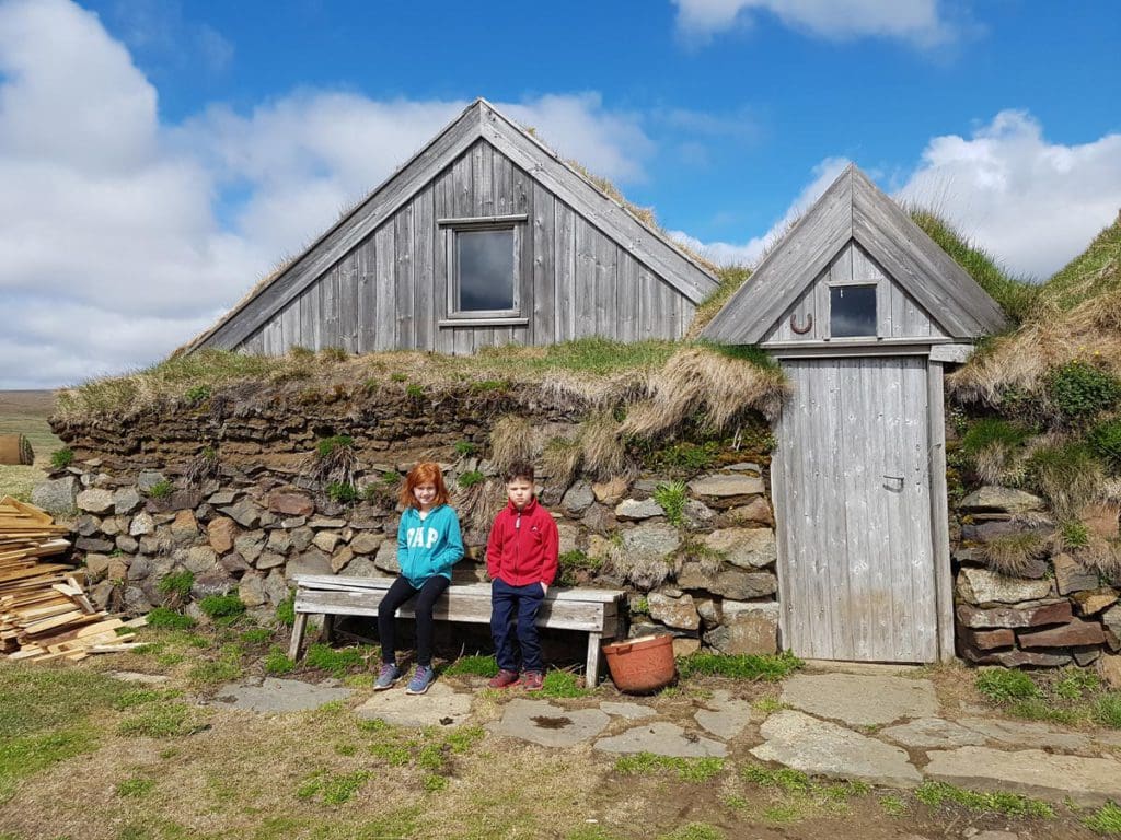 Two kids sit in front of old Icelandic huts while exploring the country.