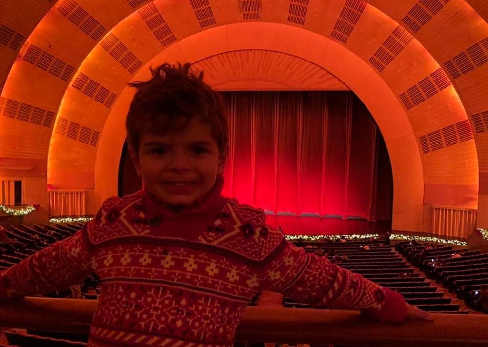 A young boy poses with a large theater stage behind him before a Christmas performance.