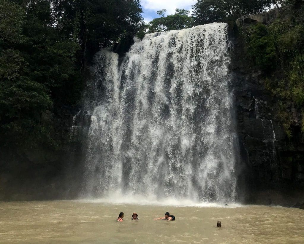 Four people swim below a waterfall at Llanos de Cortes Waterfall in Costa Rica.