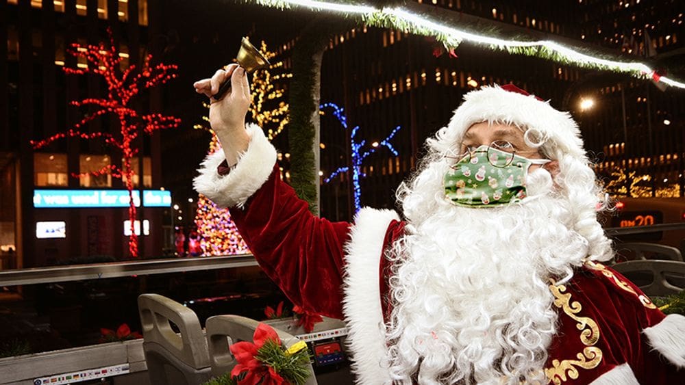 A Santa, wearing a mask, waves a bell while on the North Pole Express tour, one of the best New York City Christmas activities with kids.