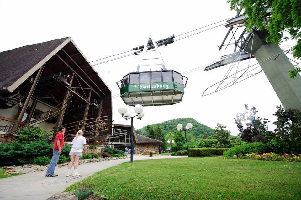 Two people stand outside a chalet, overhead the Ober Gatlinburg aerial tram glides by, one of the best things in a family itinerary for Gatlinburg Pigeon-Forge.