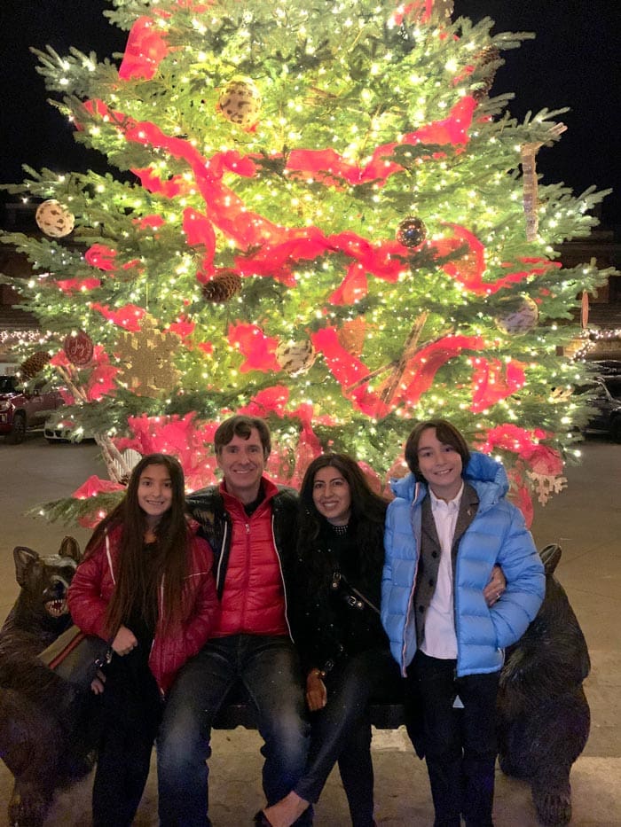 A family of four poses together in front of a large Christmas Tree.