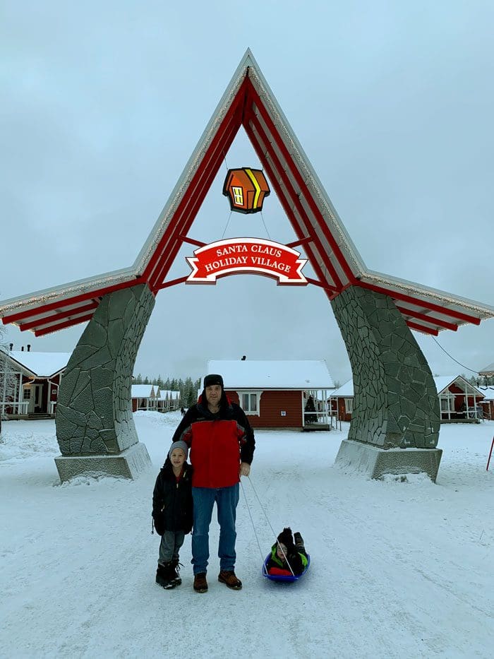 A father and his two sons pose in front of a large sign for Santa's Village.