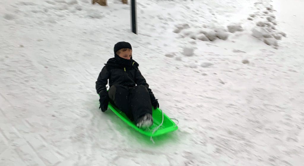 A young boy sleds down a snowy hill on a green sled, a must do on our Finnish Lapland itinerary for families.