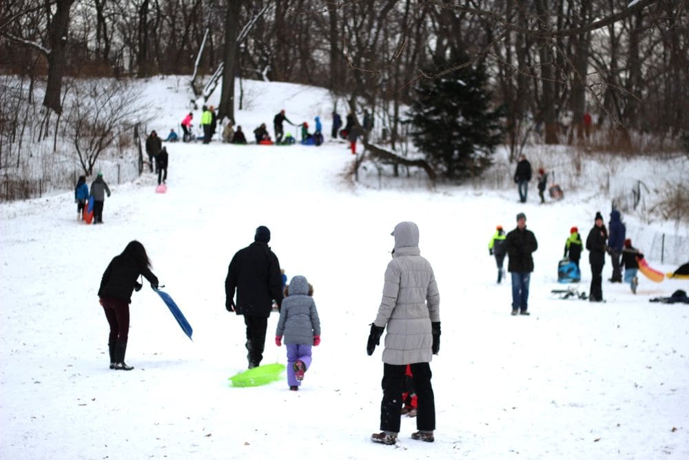 Several people enjoy fresh snow and a day of sledding at Central Park, one of the best New York City Christmas activities with kids.