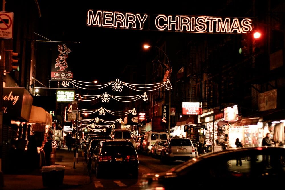 A view down a dark street in Little Italy, featuring tons of Christmas lights, including a lit sign reading "Merry Christmas".