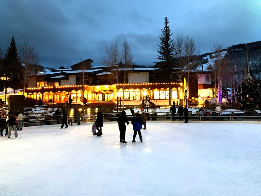 Several people skate around a rink in Vail at night.