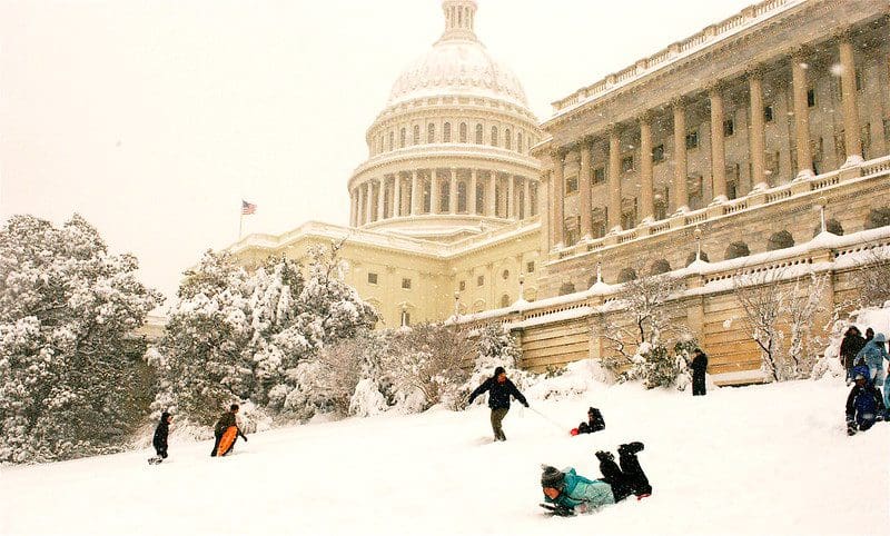 Several people sled on Capitol Hill on a snowy day in Washington DC, with the capitol building in the distance.