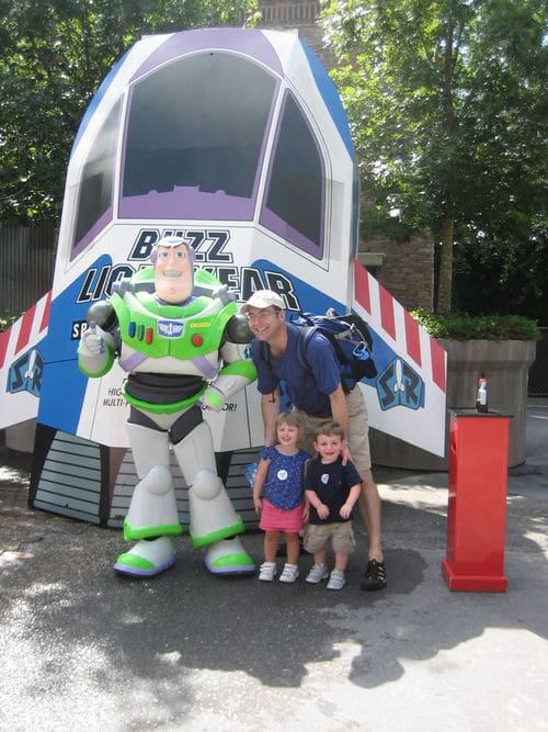 A dad and two young kids stand with Buzz Lightyear at a Disney park.