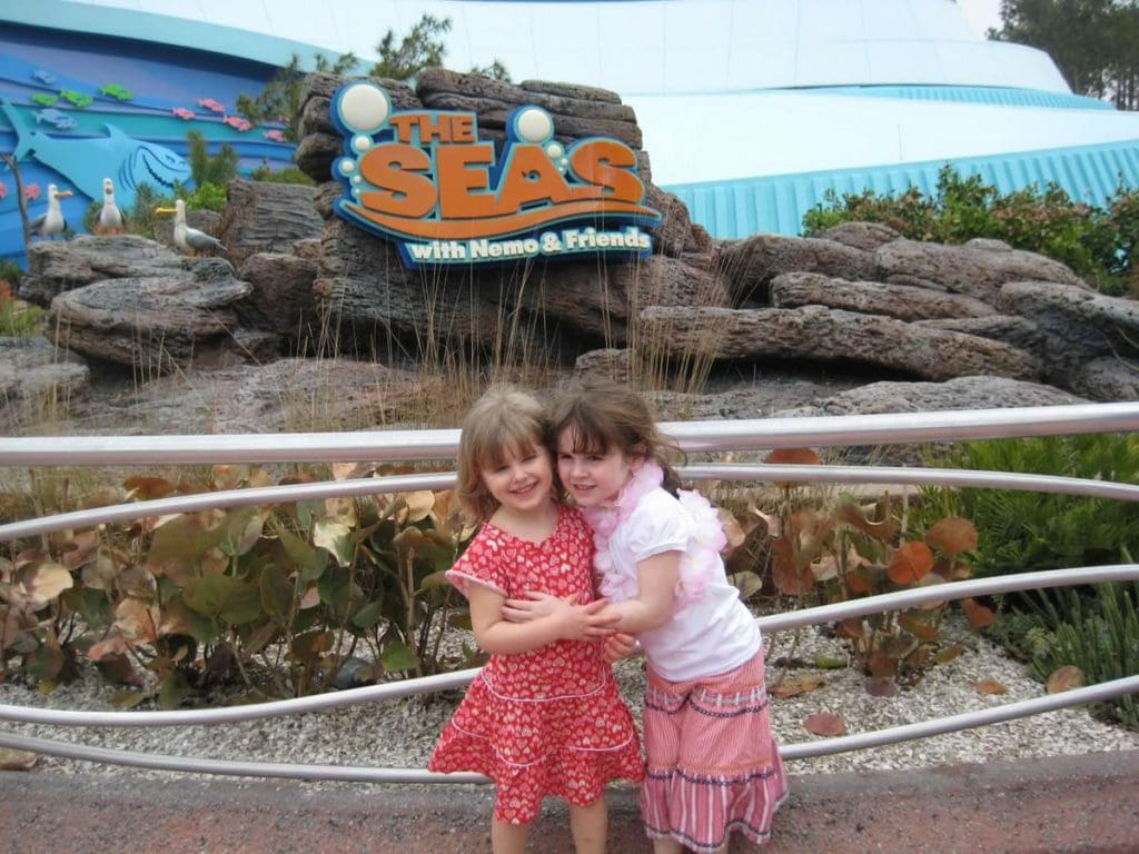 Two kids embrace in front of a sign for The Seas, a Disney attraction.