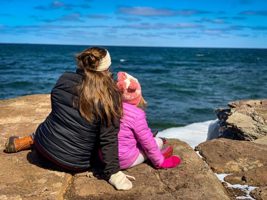 A young girl and her mom sit on a rock formation while visiting Marquette, one of the best places to visit in Michigan’s Upper Peninsula with kids.