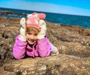 A young girl holds her hands in her face, while laying on the iconic black rocks in Presque Isle Loop in Michigan.
