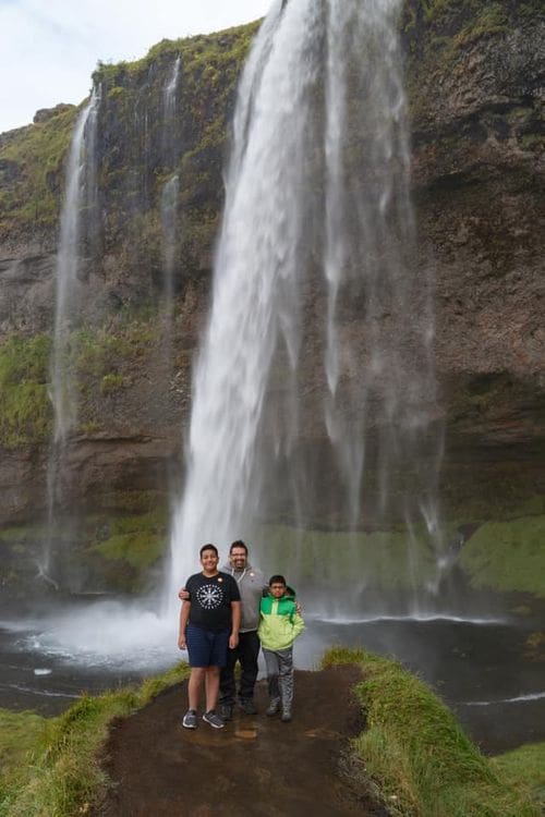 A family of three stands in front of a waterfall in Iceland.