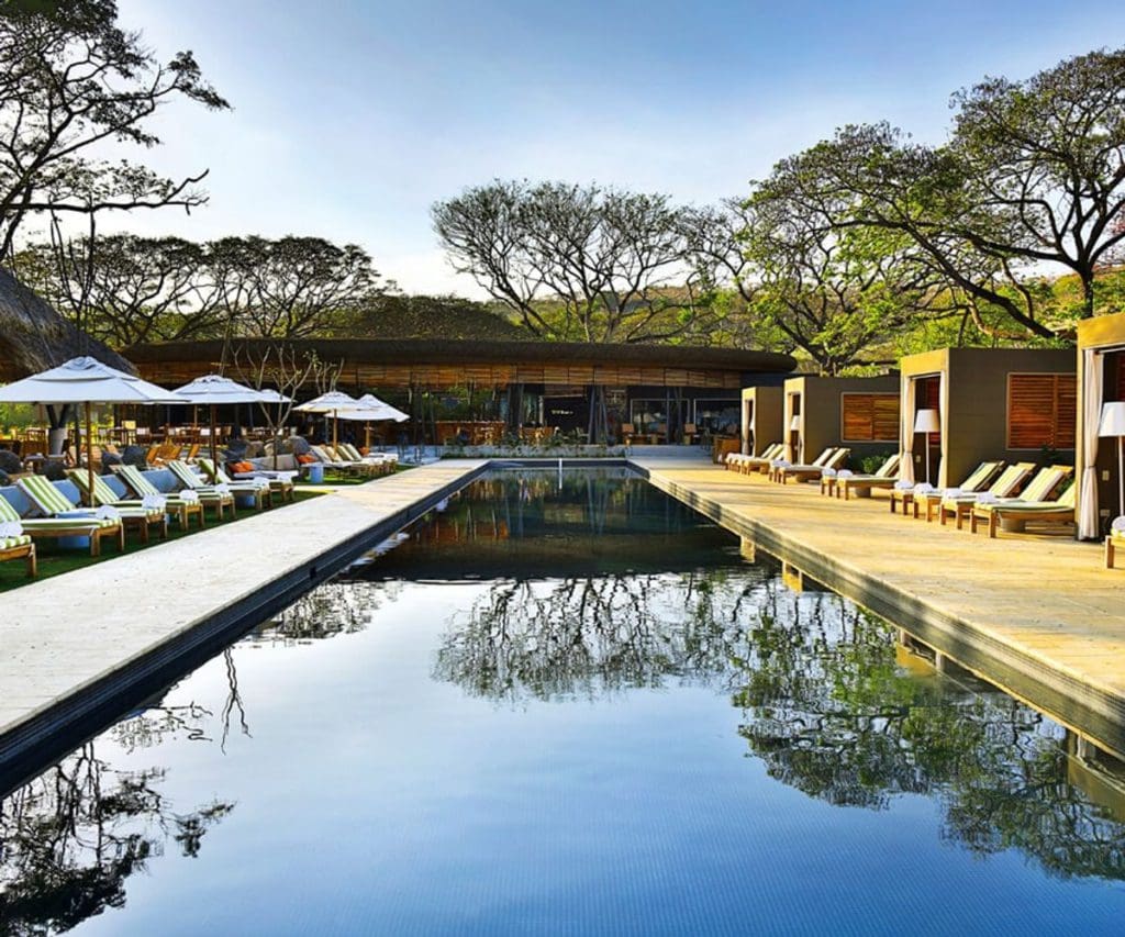 The pool at the El Mangroove, reflect trees on its calm waters, flanked by pool-side loungers on both sides.