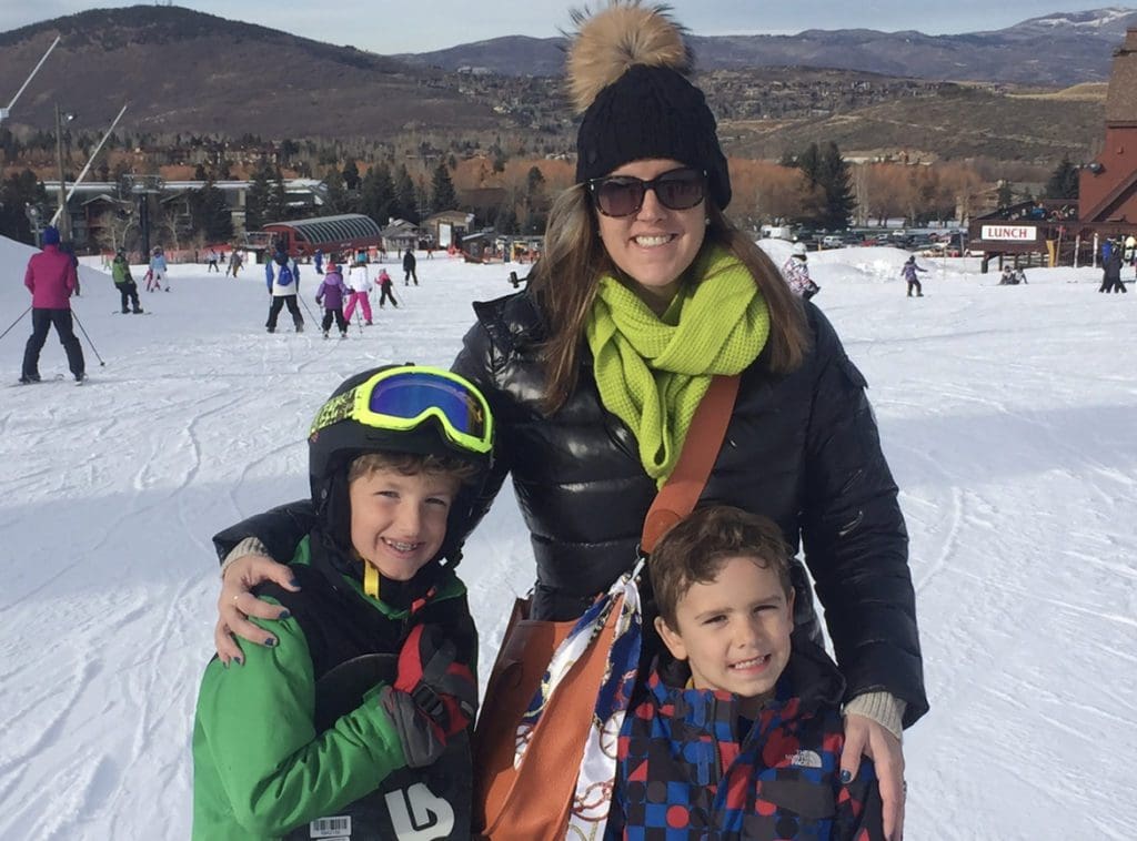 A mom and her two kids stand together smiling, while spending the day skiing in Deer Valley.