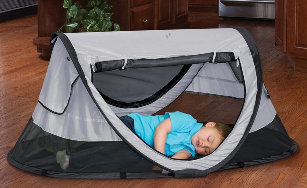 A young toddler boy sleeps inside a KidCo Peapod Toddler Travel Bed.