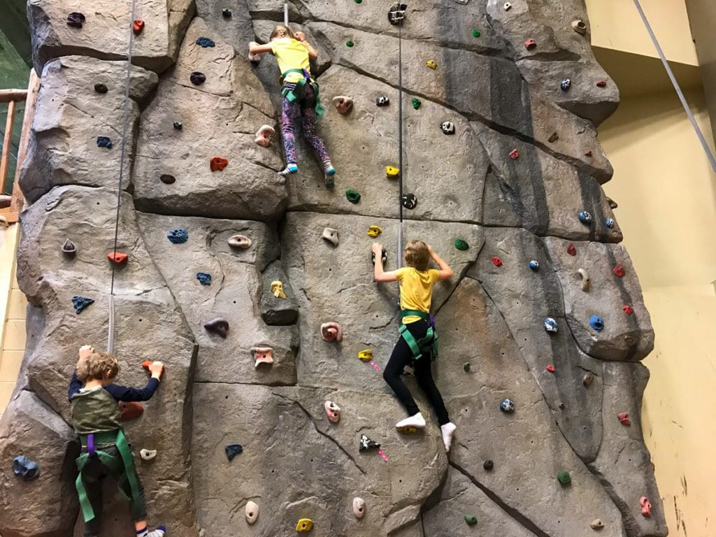 Two kids climb along the rock wall, one of the best things to do at YMCA Snow Mountain Ranch for Families.