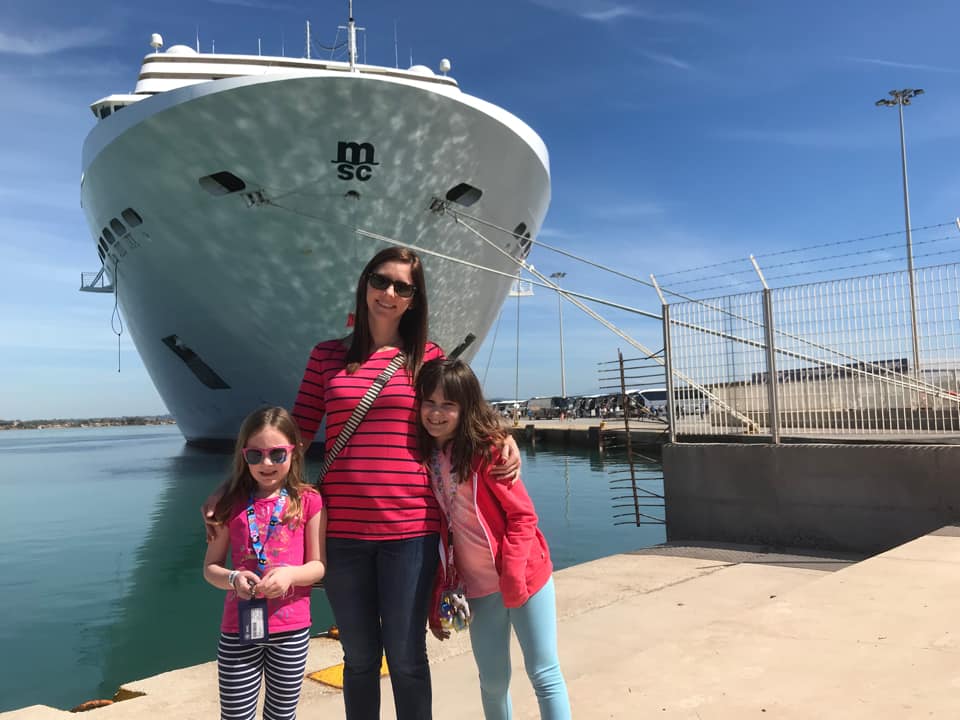 A mom and her two girls stand in front of a MSC Cruises ship, one of the best cruise lines for families.