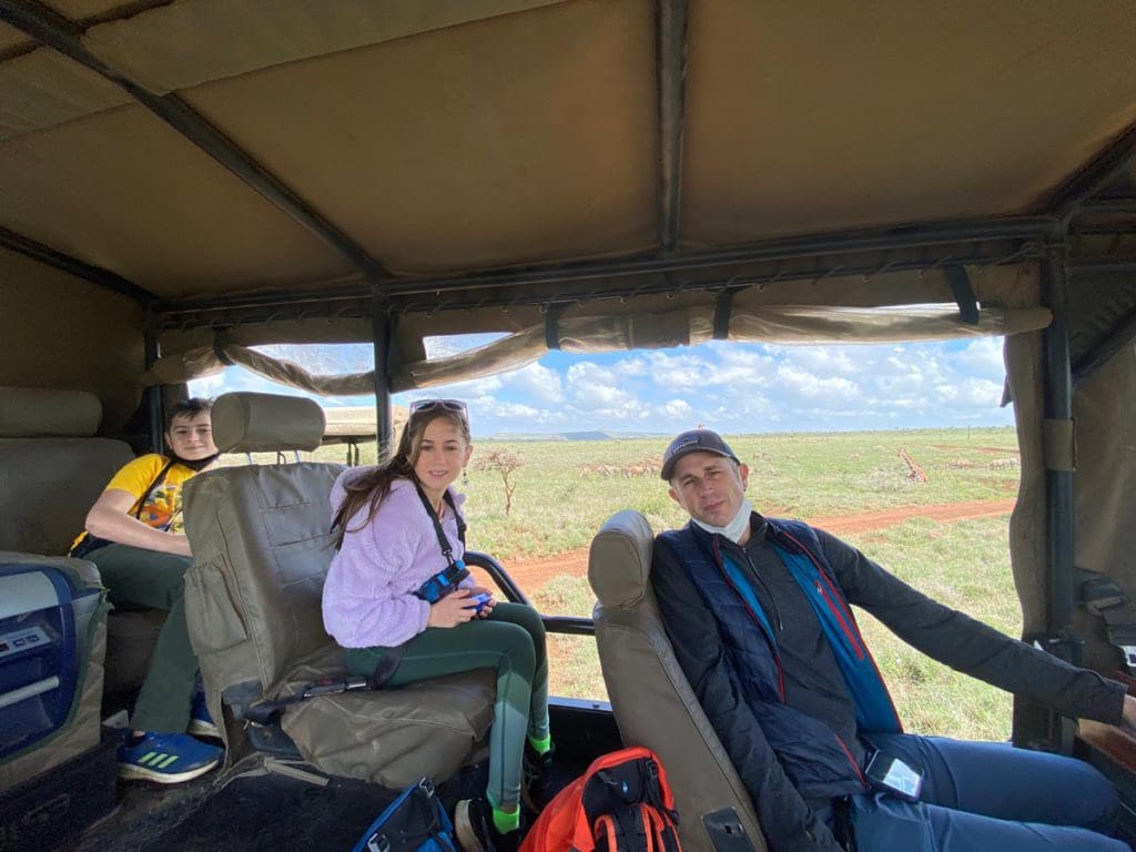 A dad sits at the driver's seat at a safari caravan, with two kids in the back seats.