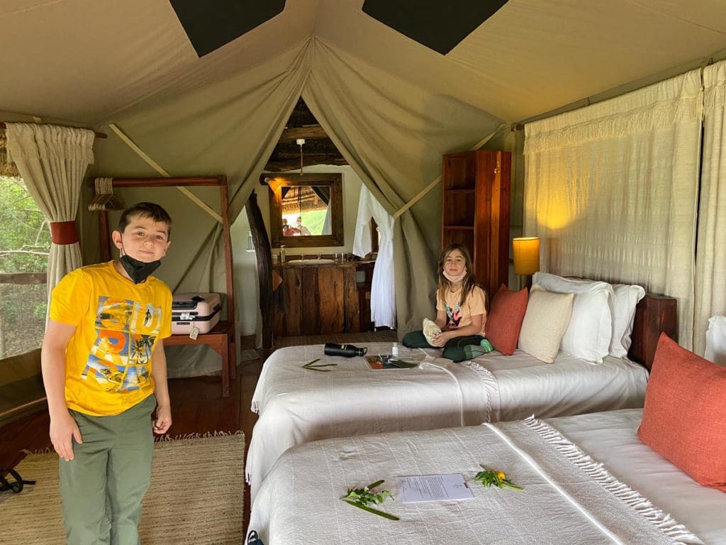 Two kids relax inside their canvass tent while on a Kenya safari as a family.