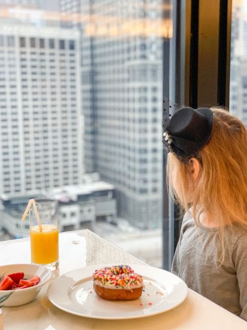 A young girl looks out onto a Chicago skyline, while eating breakfast at The Langham Club.