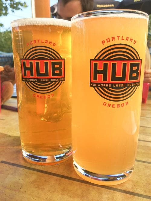 Two pints of beer sit on a picnic table, showing off the logo for Hopworks Brewery, one of the best places to eat in Portland with kids.