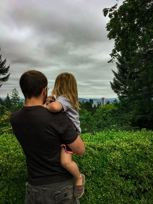 A dad hold his young daughter as they look out onto the Portland skyline.