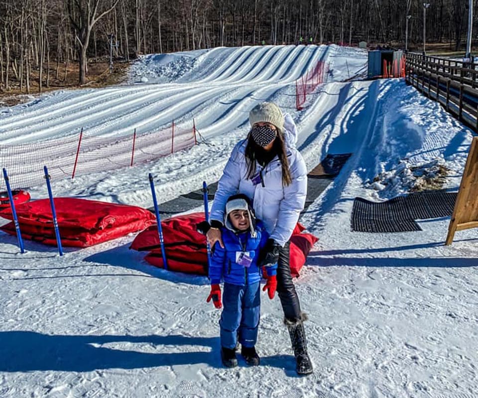 A mom and her young son stand in the snow at a snow tubing run near New York City.